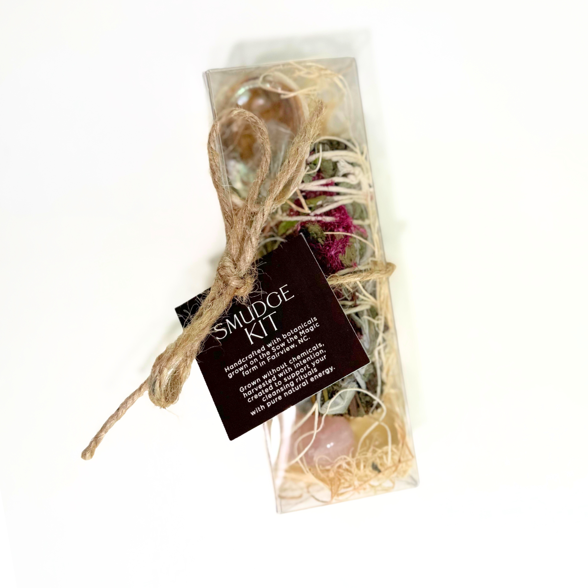 Handcrafted smudge kit with farm grown botanicals palo santo gemstones and abalone shell in clear packaging.