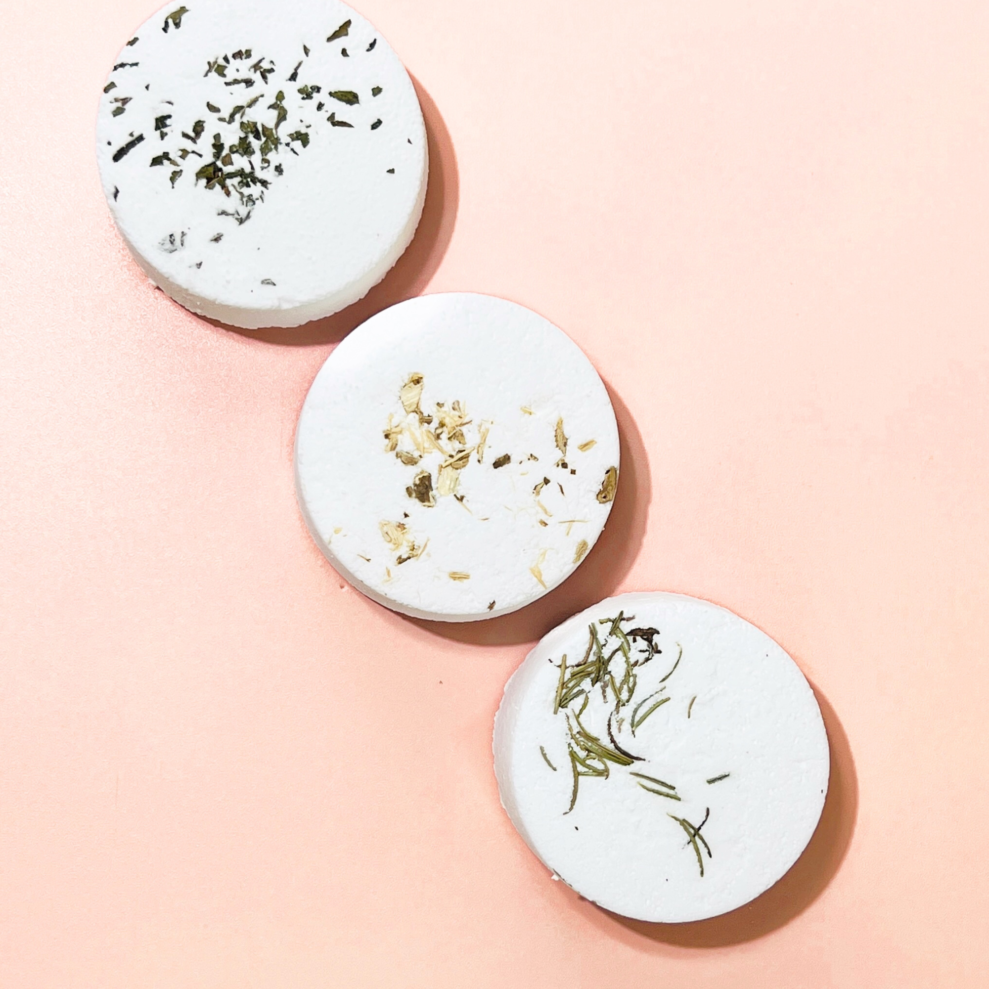 Three tarot shower steamers with peppermint, marshmallow and rosemary botanicals displayed on a peach background