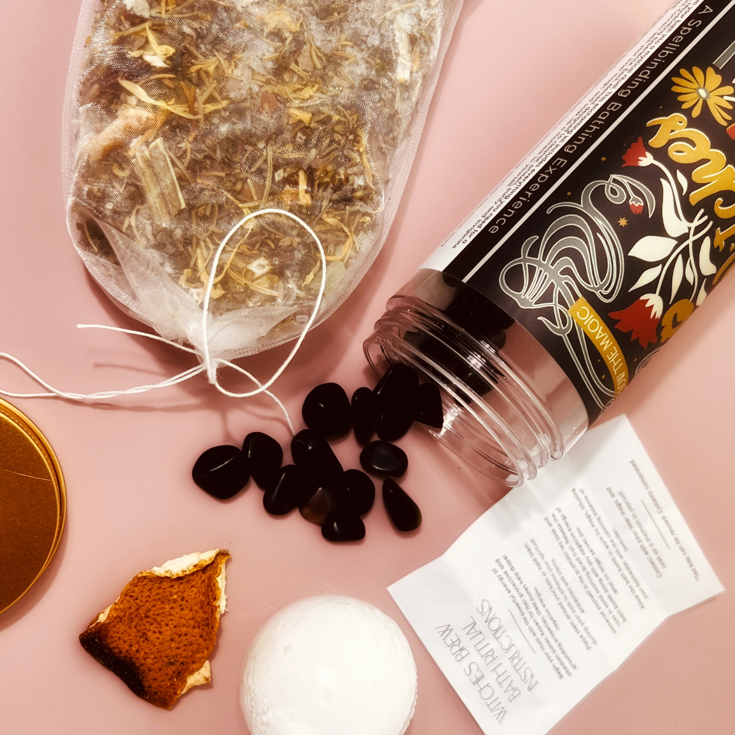 Close-up of Witch’s Brew Bath Ritual Kit with obsidian stones spilling from jar beside herbal bath soak and dried orange peel.