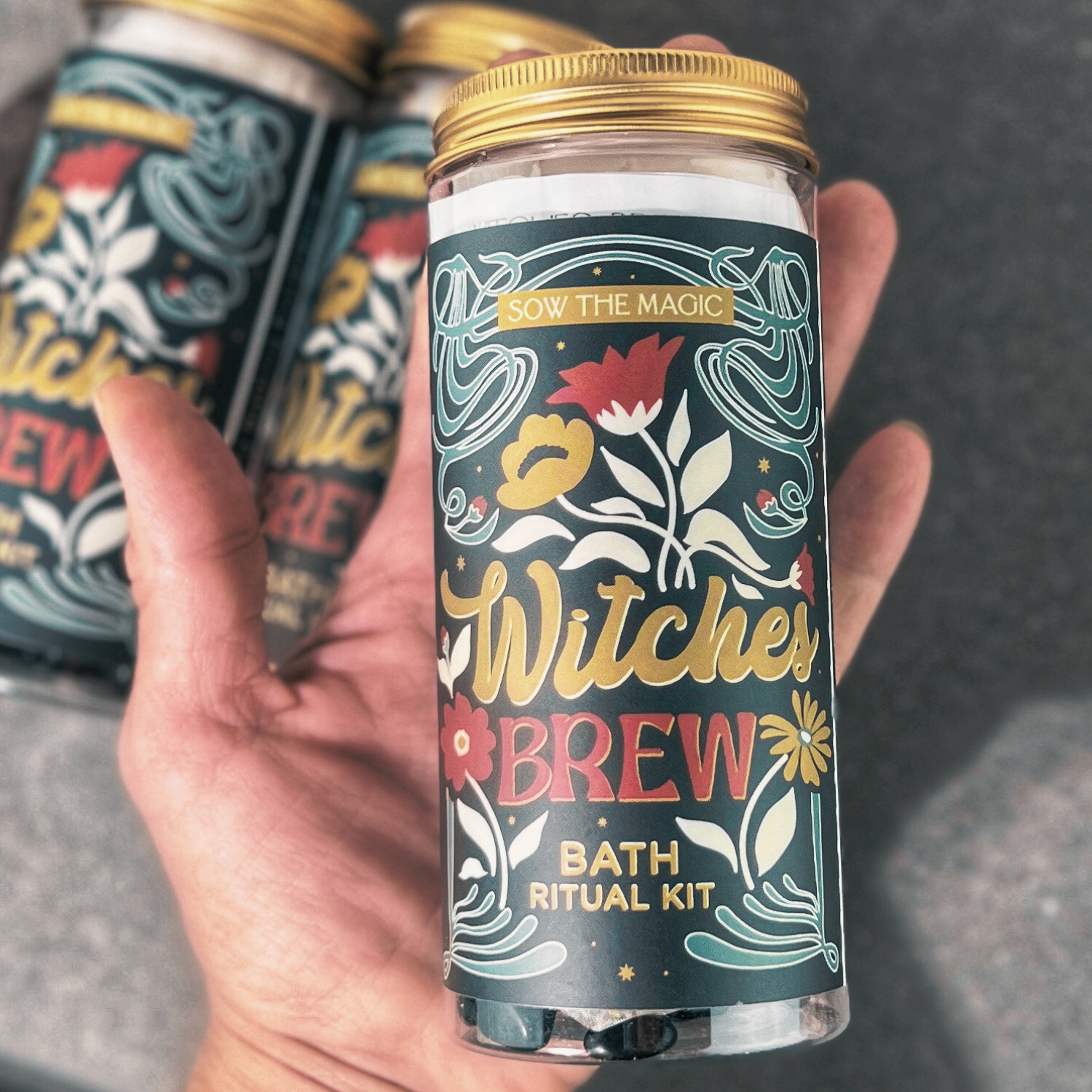 Hand holding a Witch’s Brew Bath Ritual Kit showing detailed label with golden lid and mystical floral design.