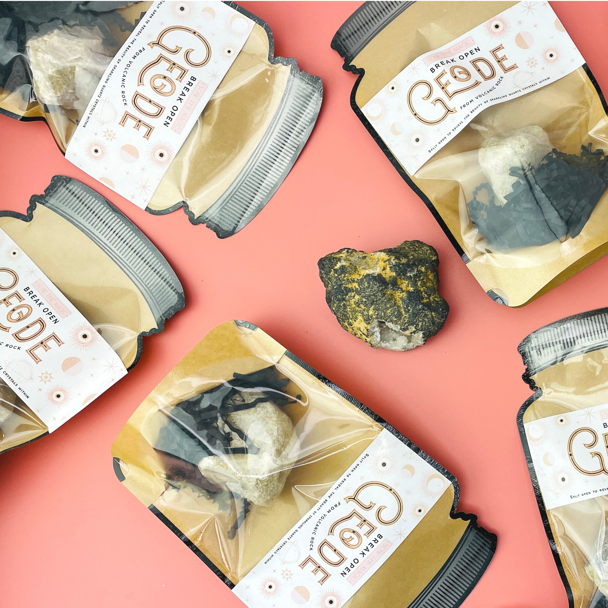 Multiple Break Open Geode Rock pouches and volcanic stones arranged on coral pink background