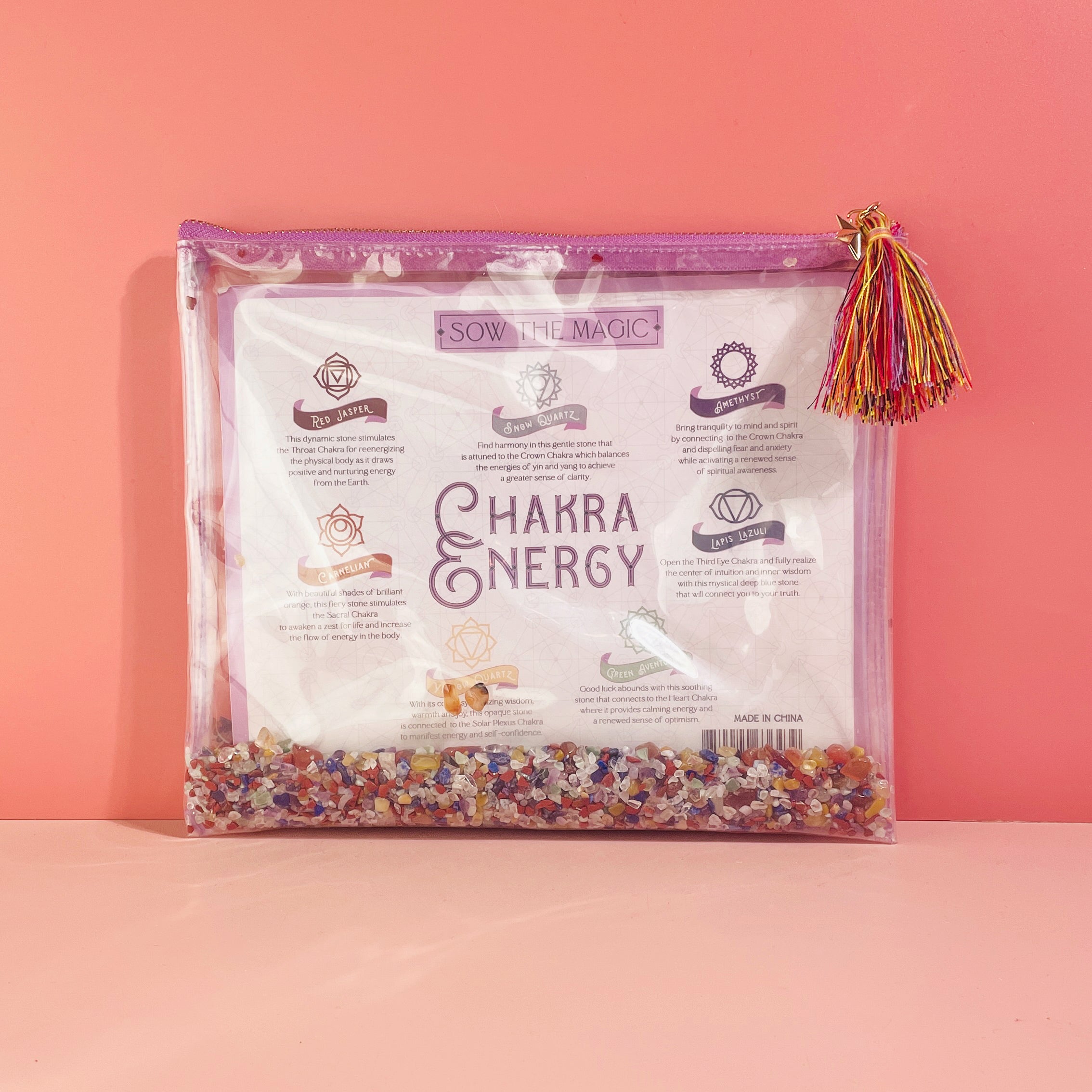 Front view of Chakra Energy Gemstone Cosmetic Bag with seven colorful healing crystals and tassel on pink background
