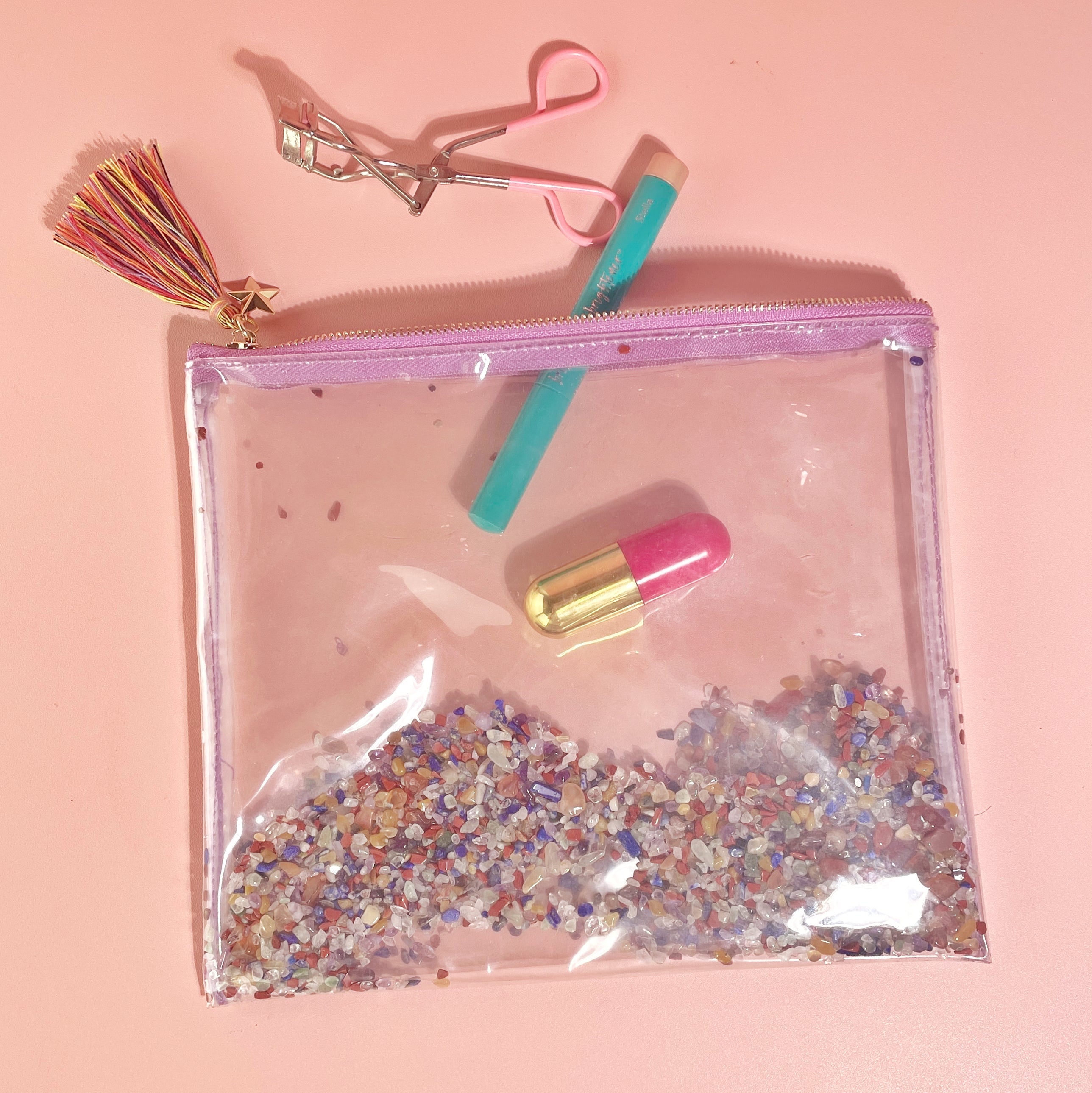 Flatlay of Chakra Energy Gemstone Cosmetic Bag with makeup items and gemstone mix on pink background