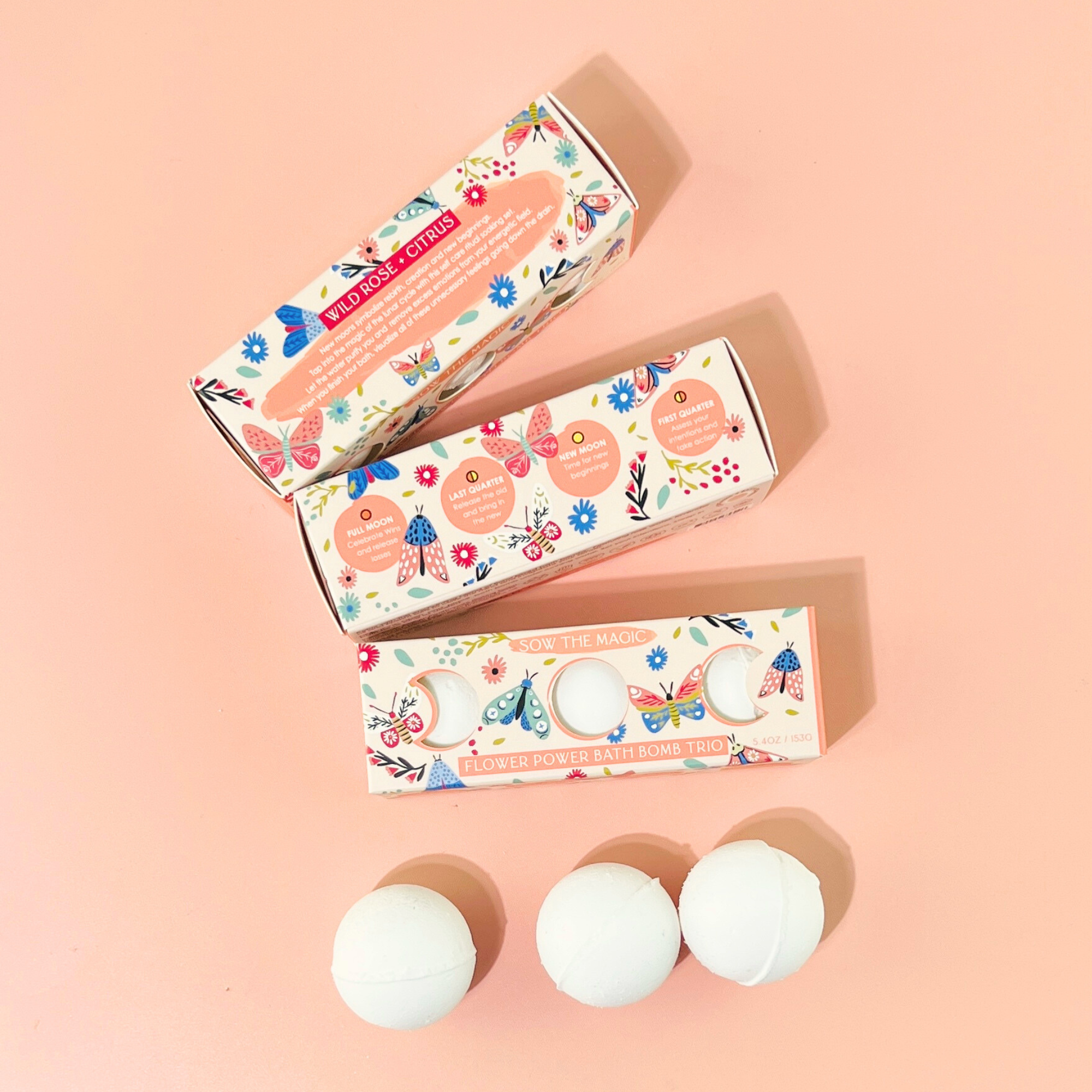 Three Flower Power Bath Bomb Trio boxes displayed with white bath bombs on pink background