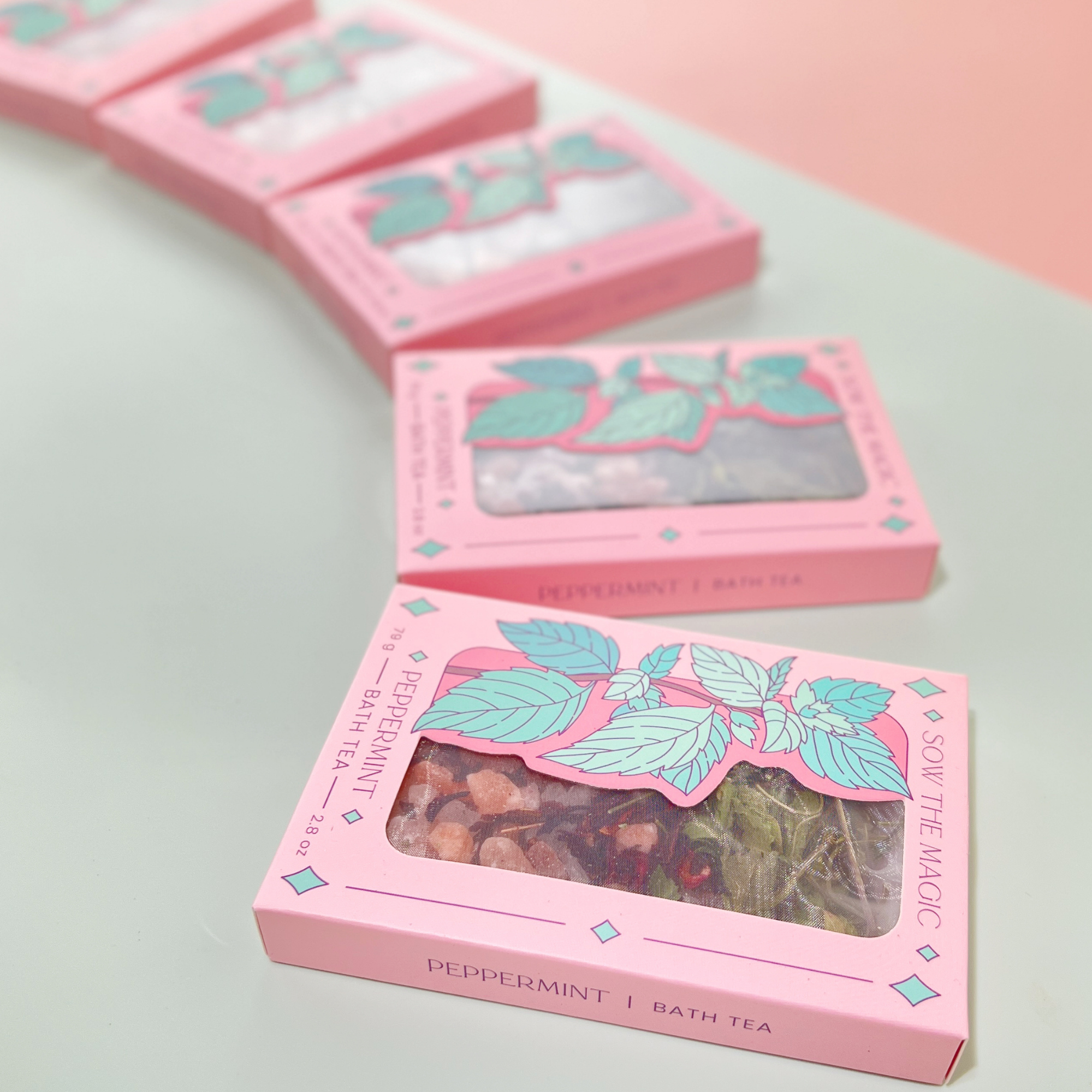 Row of Peppermint Tarot Botanical Bath Tea Boxes displayed diagonally on mint and blush background with soft light.