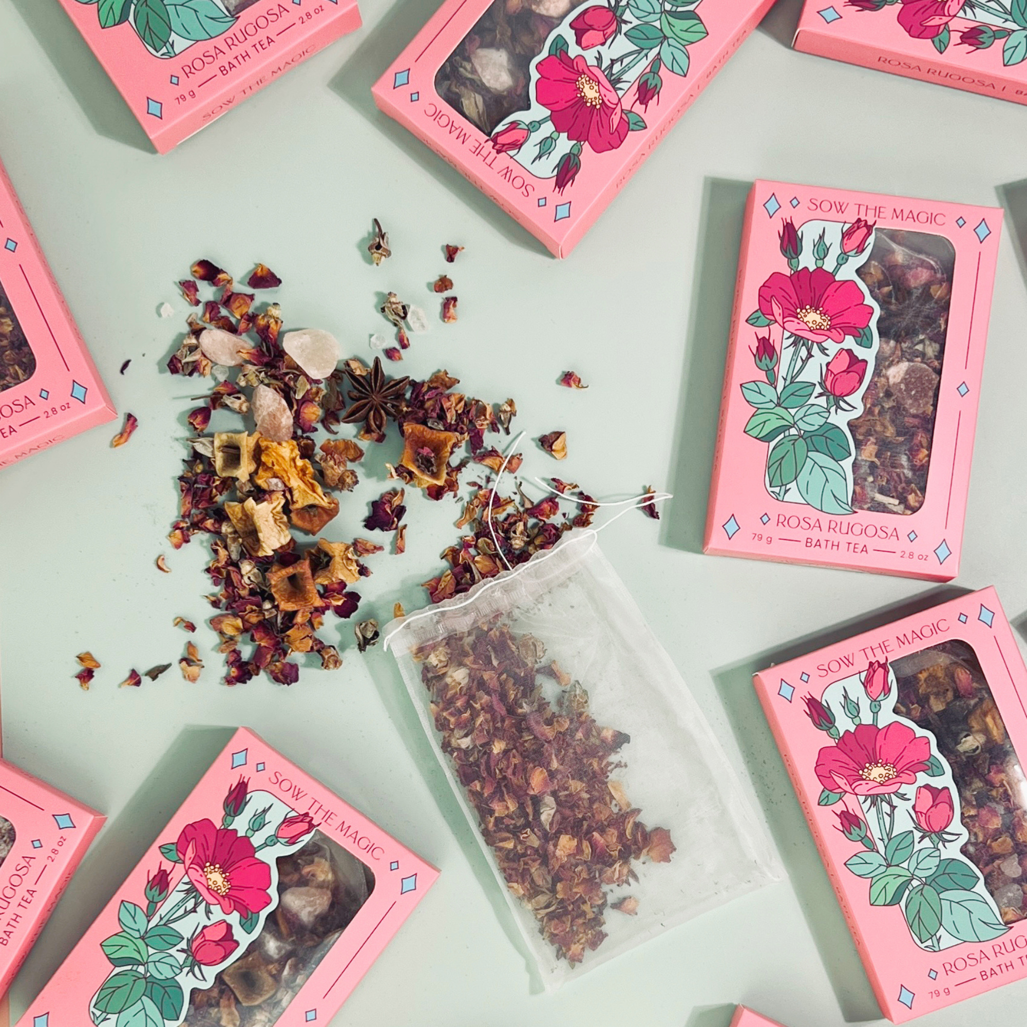 Flatlay of Rosa Rugosa Tarot Botanical Bath Tea Boxes by Sow the Magic with rose petals and herbs arranged artistically.