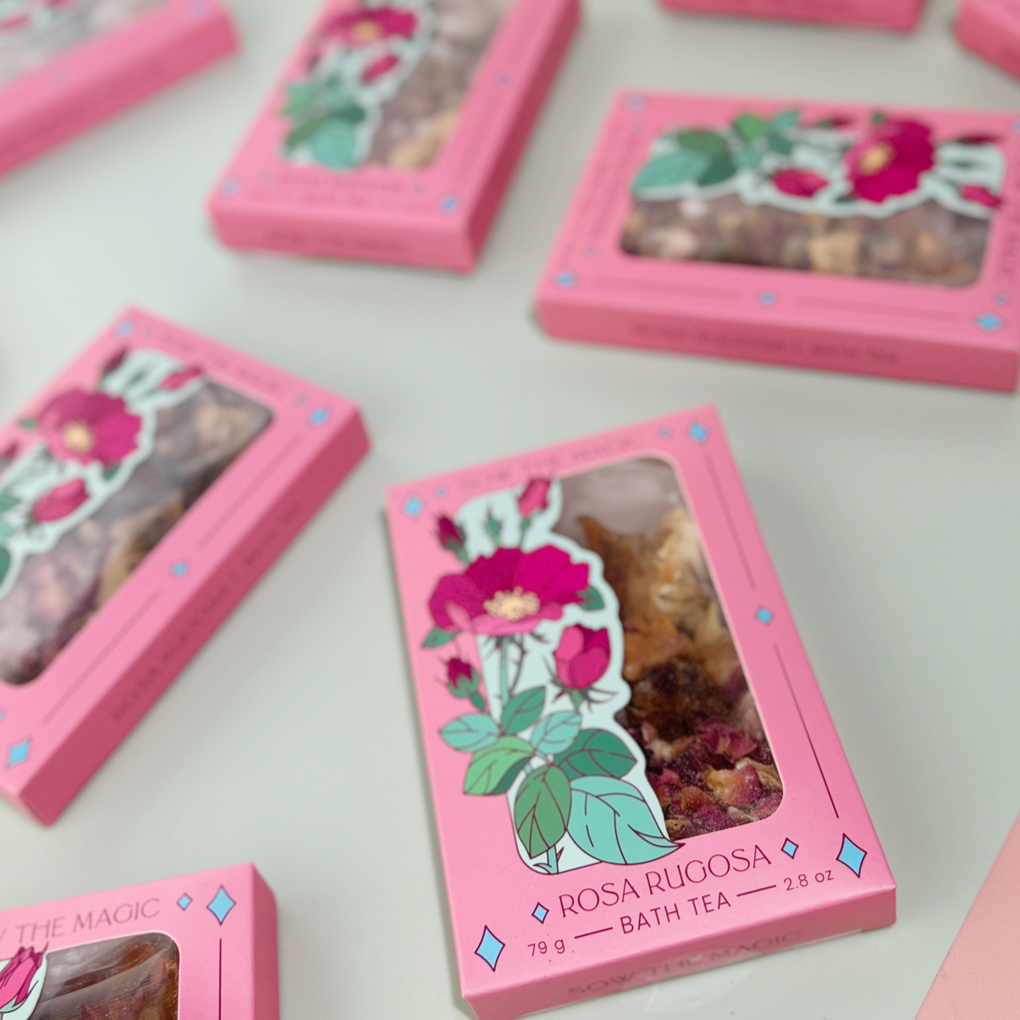 Multiple Rosa Rugosa Tarot Botanical Bath Tea Boxes by Sow the Magic arranged on pastel surface with rose illustration and window packaging.